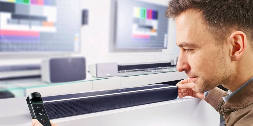 A man uses a laser device to measure the length of his sound bar speaker