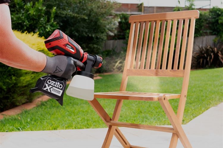 Person spraying chair with outdoor paint spray gun