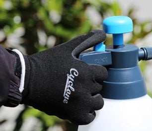 Person watering garden wearing gardening gloves
