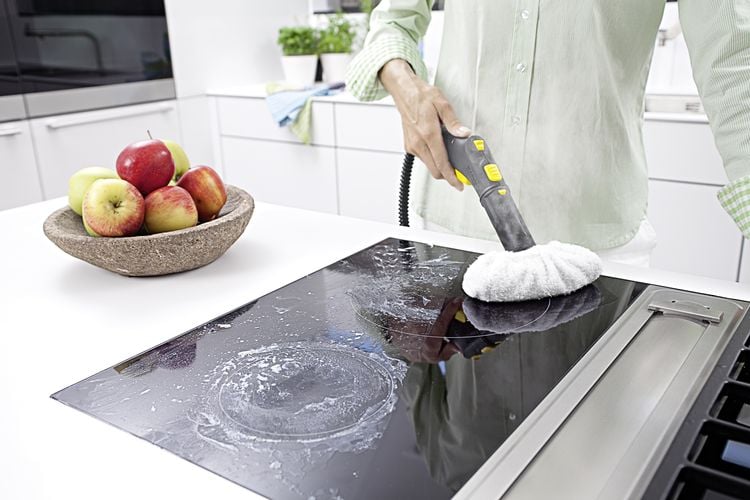 Person using handheld steam cleaner to clean induction cooktop