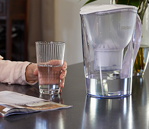 Person holding glass of water next to water filter jug