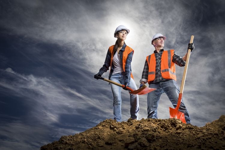 Two people with shovels on top of pile of soil