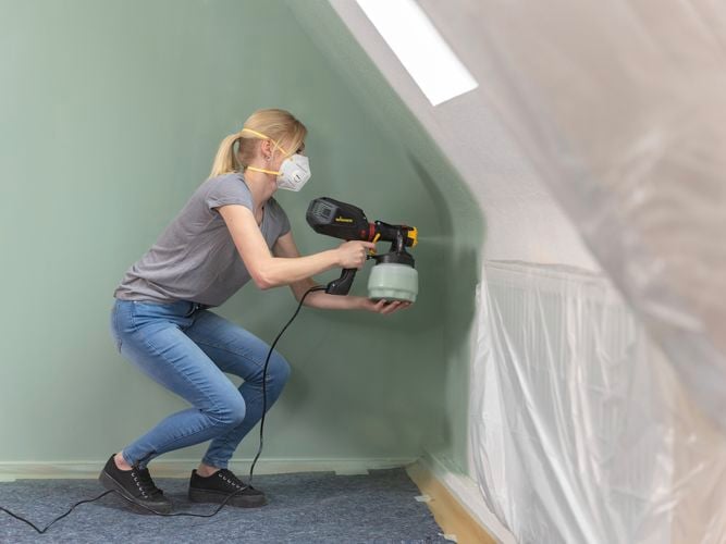Wagner
  Flexio W575 with i-Spray attachment spraying olive green paint to a curved
  wall inside a home