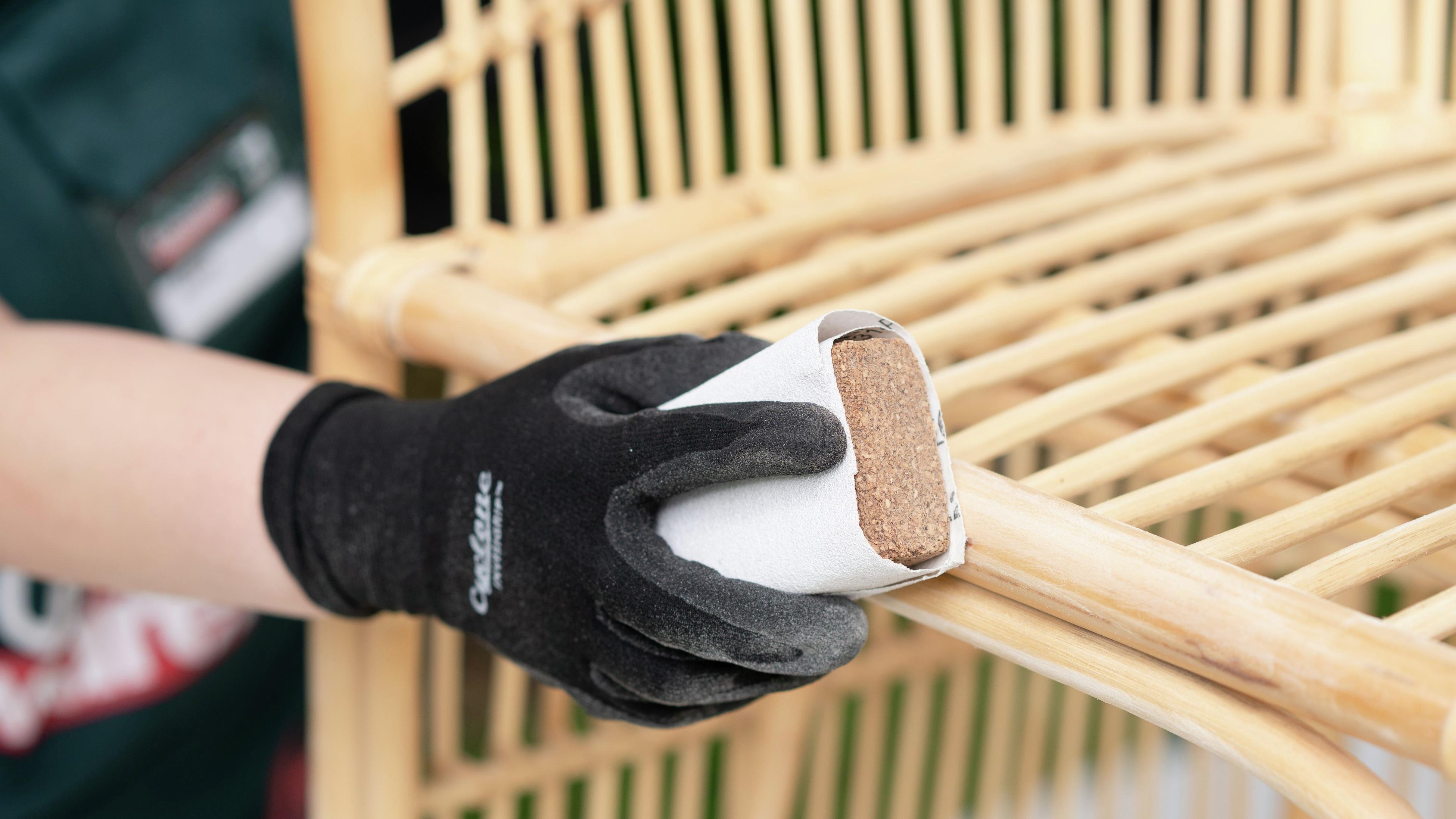 Person wearing safety gloves while sanding the wicker chair with sandpaper and sanding block.