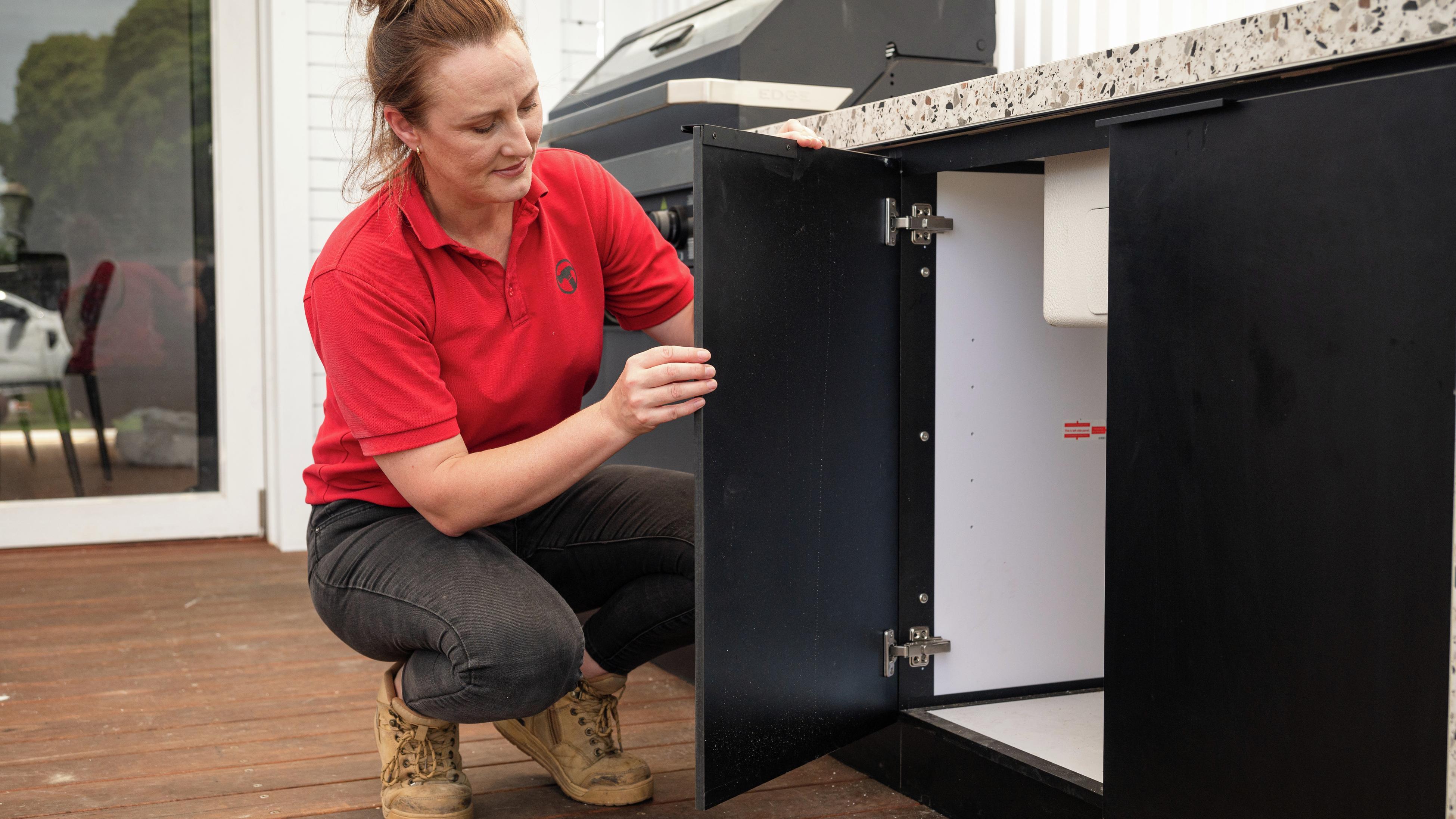 A woman opening a cupboard in an outdoor area.