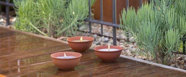 Three insect repellent candles in bowls on a deck