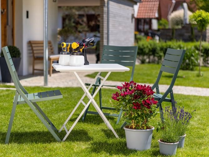 Wagner
  Flexio W575 with i-Spray and Standard Spray attachment sitting on outdoor
  furniture set after chairs have been painted in greeen