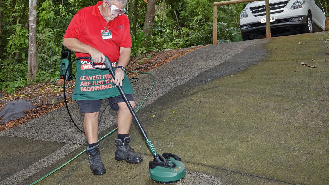 A person cleaning a driveway using a patio cleaning nozzle on a high-pressure washer
