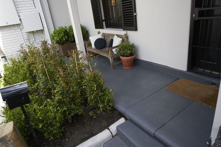 A wooden two seater lounge chair on a back porch overlooking a garden bed