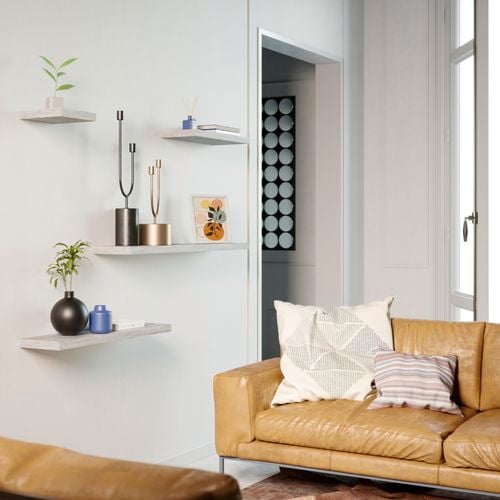 Floating shelves on a wall with ornaments, leather look couch and cushions.