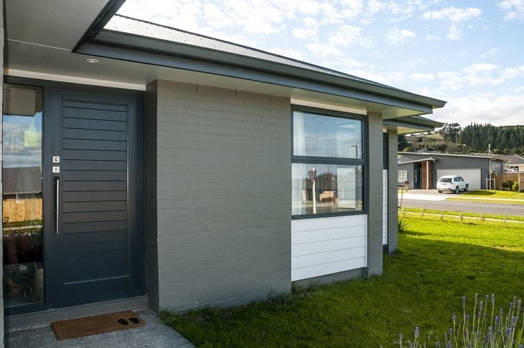 Exterior of a brick house painted mid-grey with a dark grey front door.