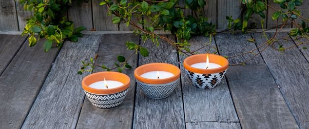 Three insect repellent candles in bowls on a deck