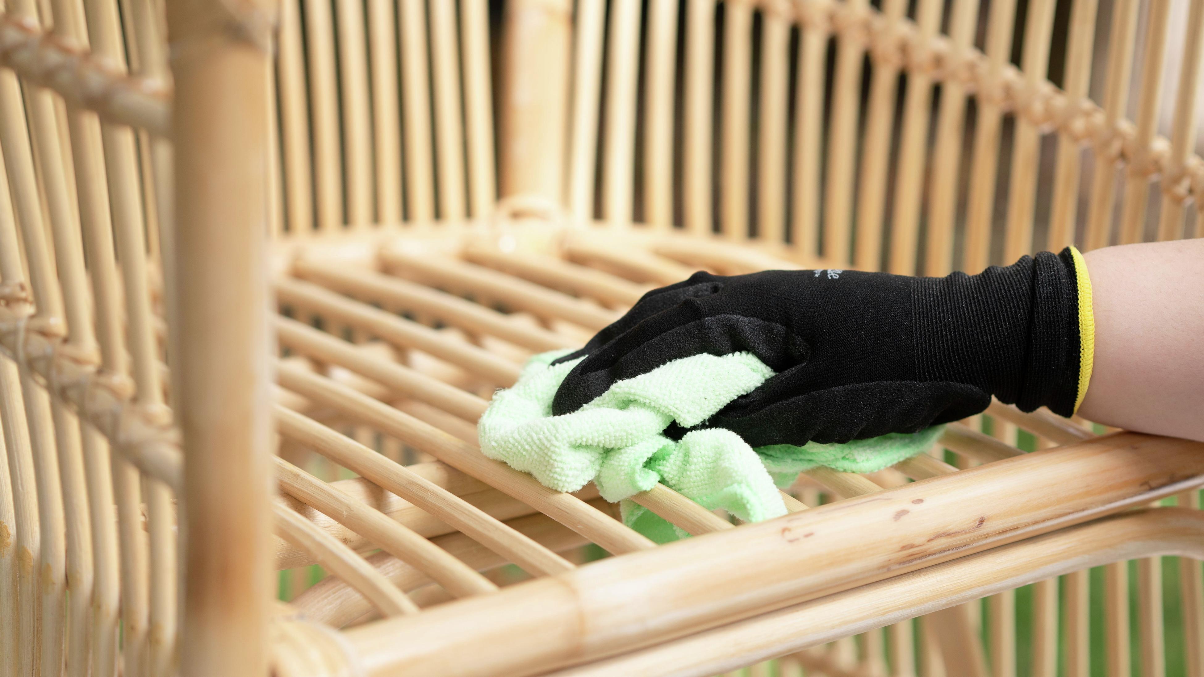 Person wearing safety gloves and removing dust off the wicker chair with a microfibre cloth