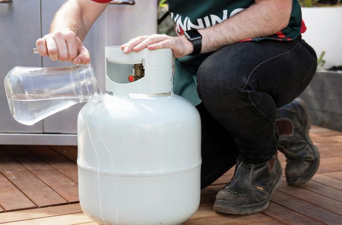 A person pouring a jug of hot water over a gas bottle