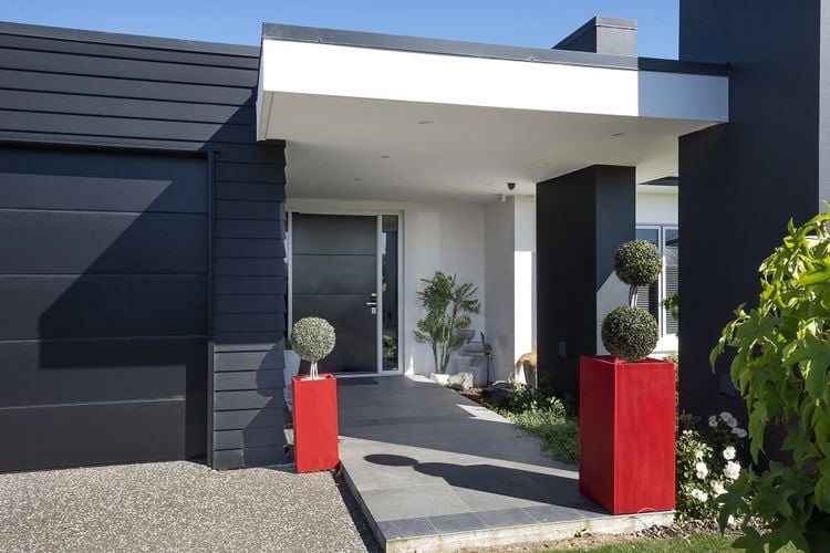 Exterior of a house painted black and white with two red planters and a dark grey front door.