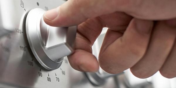 Close up of a person turning a stove knob.