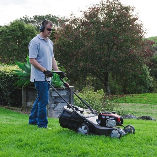 Man mowing lawn with powered push lawnmower