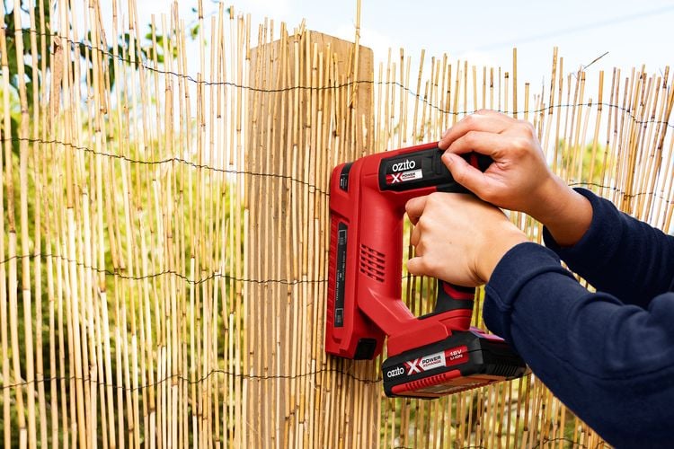 Person using nail gun to staple bamboo fencing to post