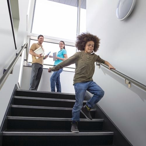 A child running down the stairs holding onto a rail