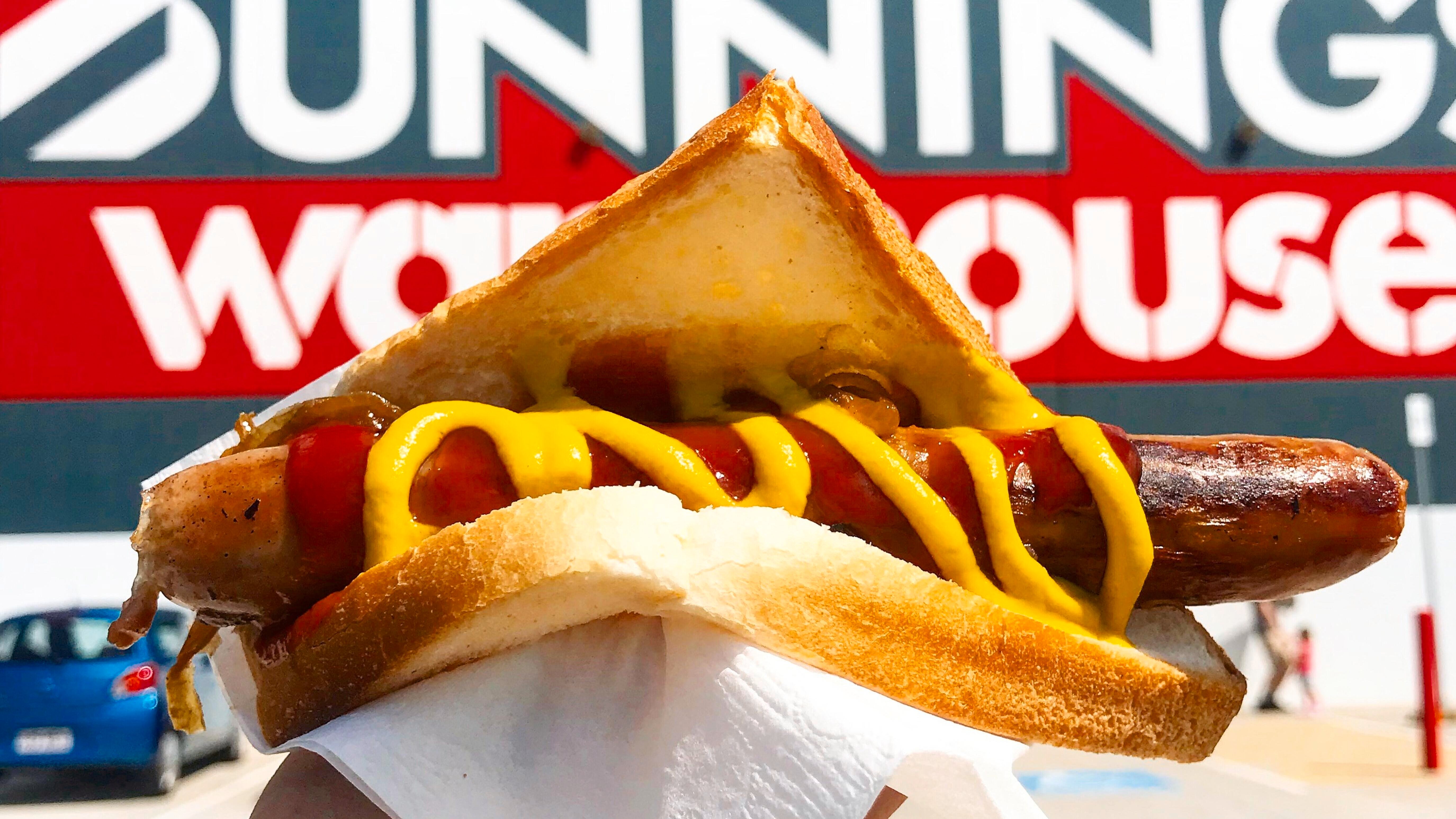 A sausage in bread with sauce on it in front of a Bunnings store