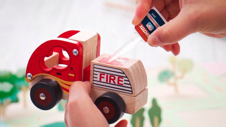 A person applying Loctite glue on a wooden toy.
