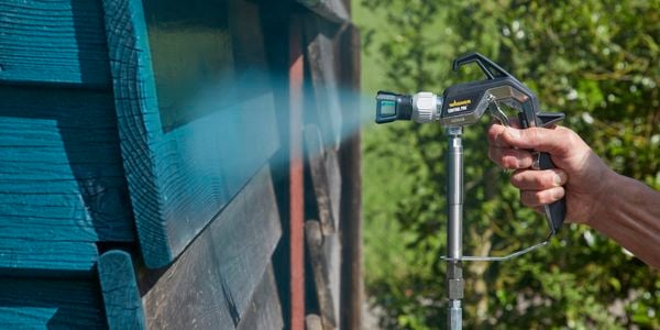 Wagner sprayer being used to spray old timber shed with blue paint to add pop of colour