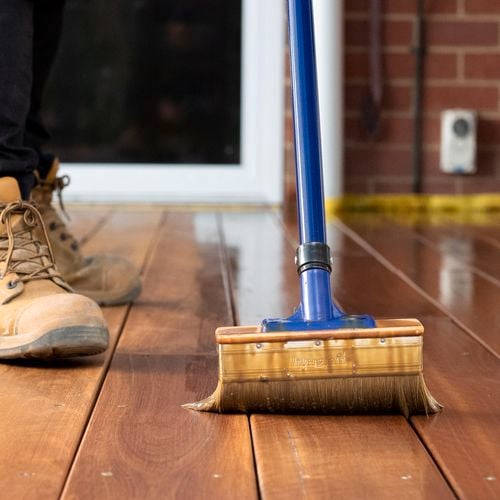 Person applying decking oil to timber decking with an applicator
