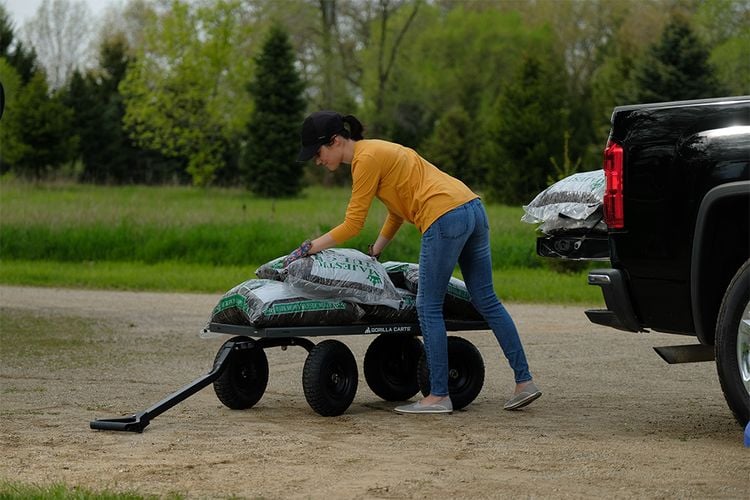 Woman unloading bags of soil from back of ute onto cart