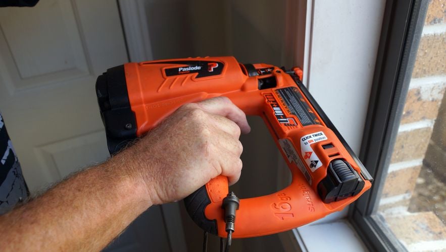 Person nailing timber window frame to wall using nail gun