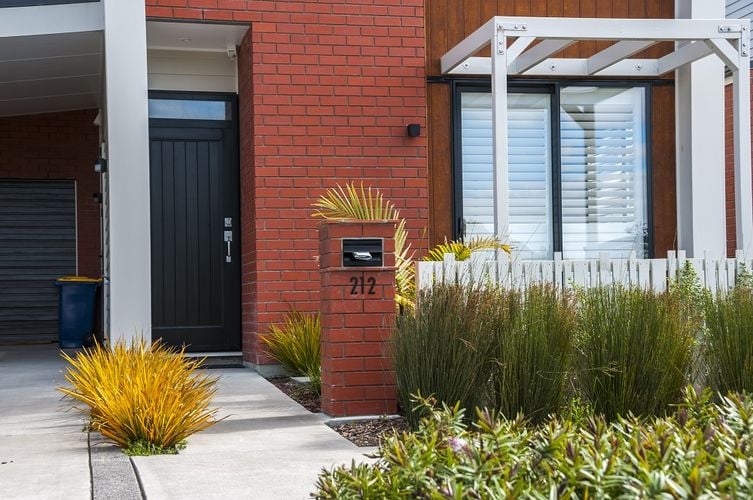 Front entryway to red brick home with white fence and carport