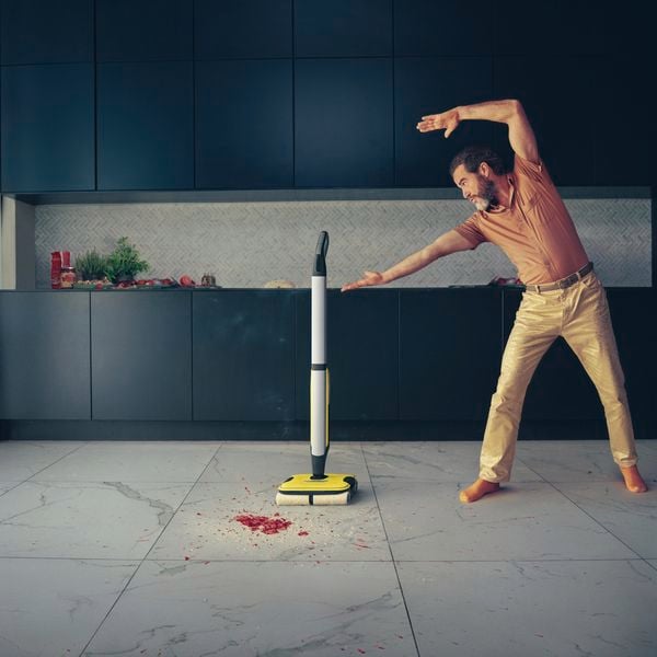 A man standing alongside the FC7 Karcher Hard Floor Cleaner with a mess spilt on the tiles in the kitchen.