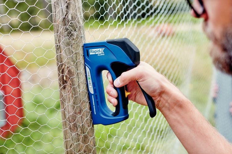Person stapling chicken wire to wood post