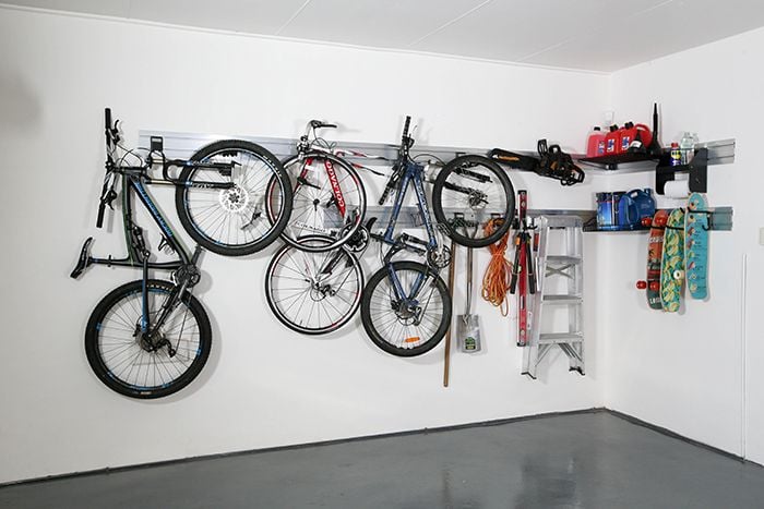 Three bikes, two skateboards, a ladder and other items hanging from hooks in a wall mounted rail