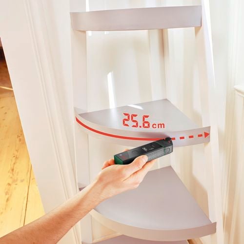 A laser device measures the curved distance of a tiered corner shelf
