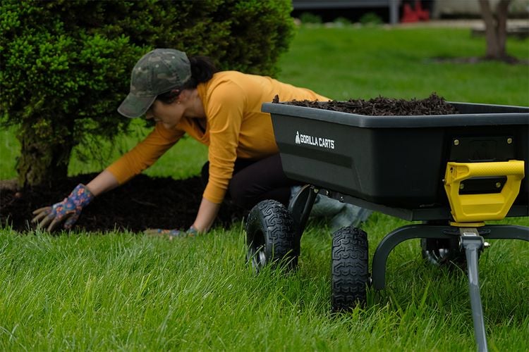 Woman placing mulch next to cart full of mulch