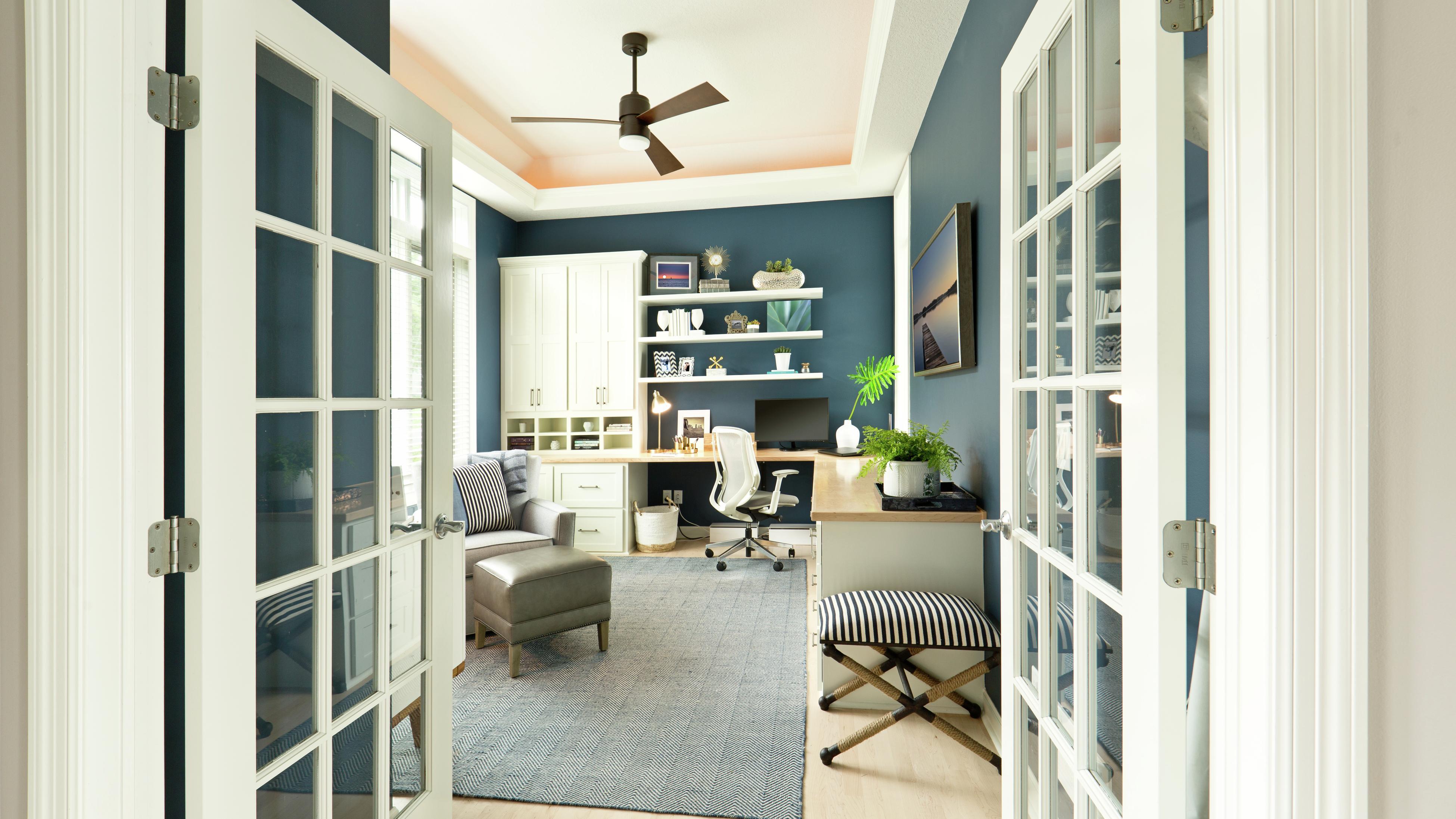 Contemporary study/office space featuring blue walls, timber built-in desk and a black ceiling fan