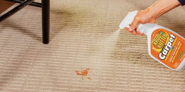 Person spraying Krud Kutter Carpet Cleaner onto orange stain on beige carpet