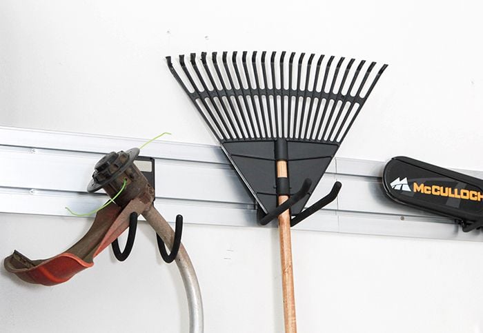 Close up of garden tools hanging from storage hooks on a wall mounted rail