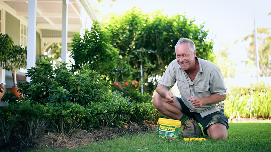 Man kneeling on grass with bucket of fertiliser at his feet