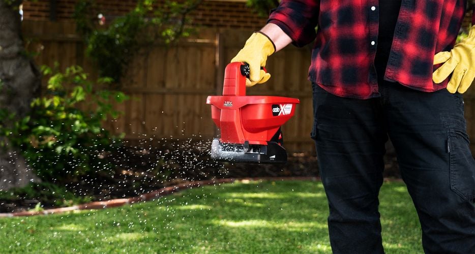 Person using seed and fertiliser spreader on turf