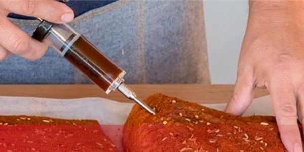 Close-up of man using a Char-Griller marinade injector on a piece of meat