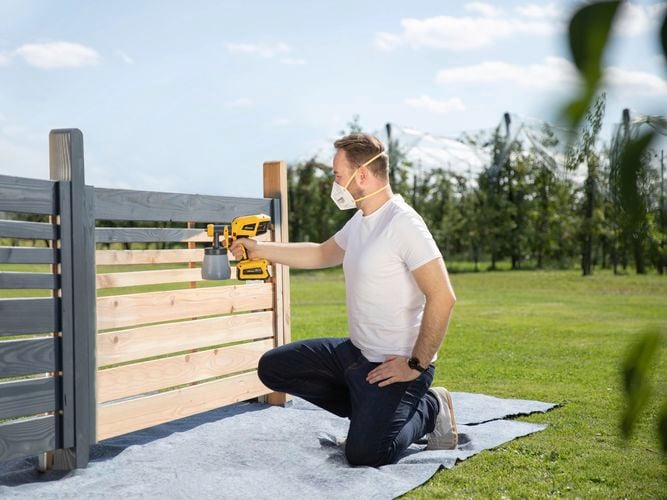 Wagner
  Cordless Flexio W600 spraying gray paint on a wooden fence outdoors