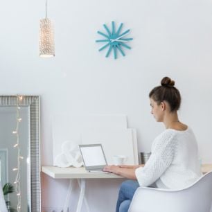 Woman sitting at desk working on laptop underneath a light with a shade