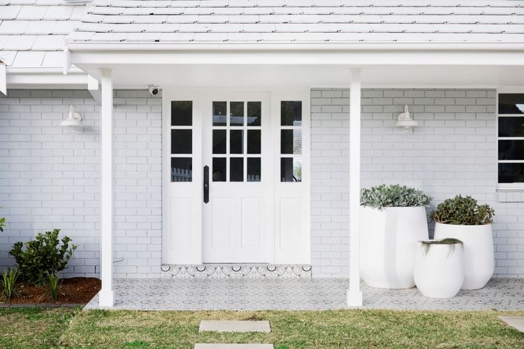 Entry to home with white door with small windows, large pot plants and garden