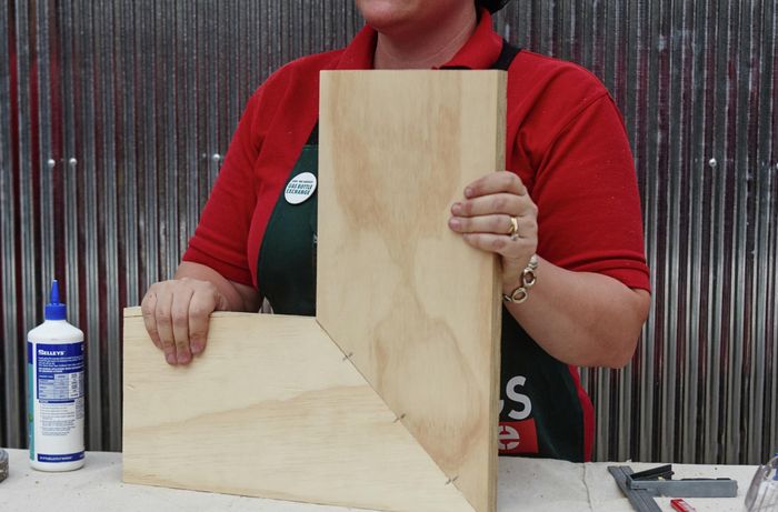 An assembled corner shelf, yet to be painted, held by a Bunnings team member