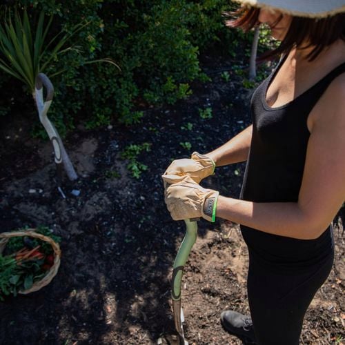 Person gardening holding a shovel in the soil and wearing gloves