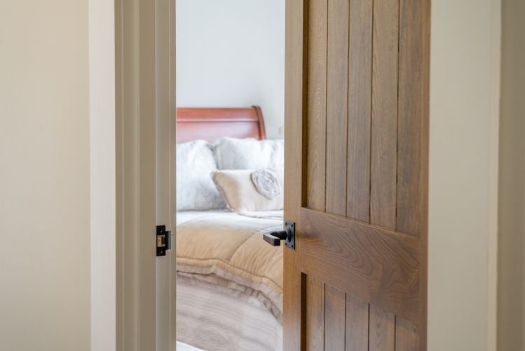 Entryway into bedroom with double bed and a thick wooden door with black handle