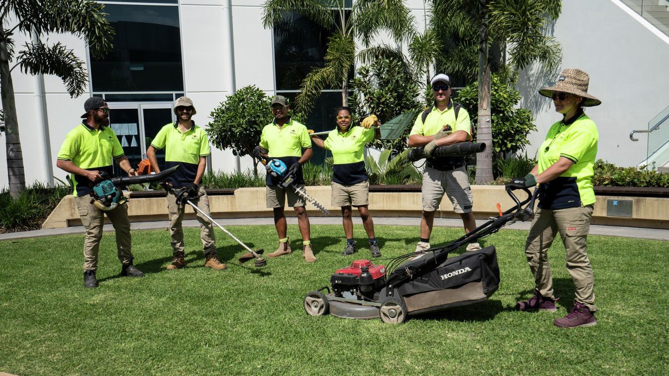 A team of landscapers with various tools of the trade, standing on a mown lawn