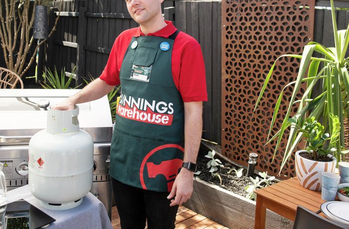 A person standing beside a gas bottle next to a BBQ