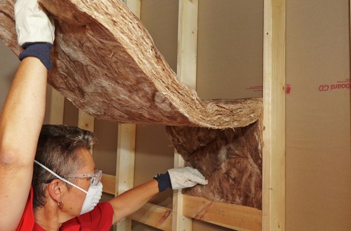 A person inserting an insulation batt between studs on a wall